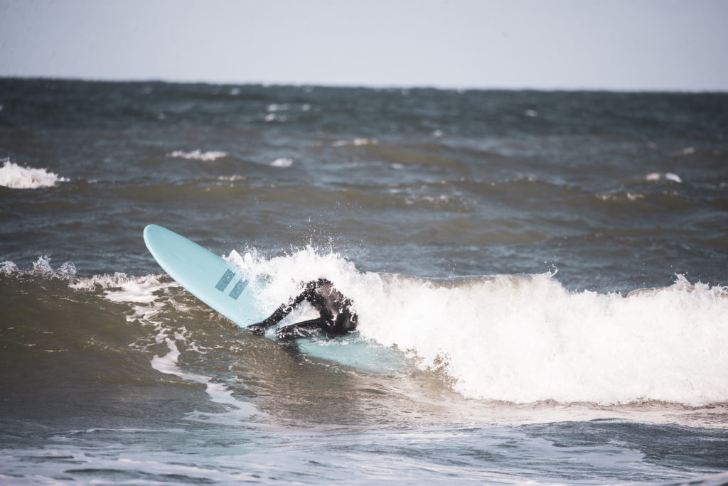 Person på surfebrett dukker gjennom bølge