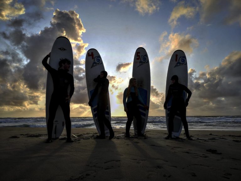 Fire ungdommer poserer med surfebrett i solnedgang