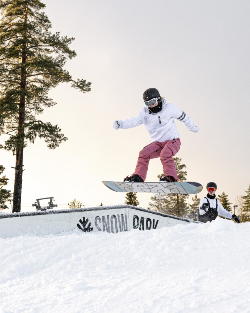 Ung kvinne hopper mot en rail på snowboard