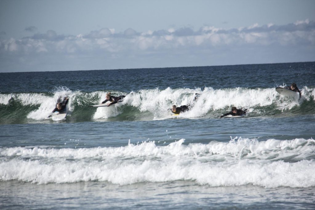 Surfere ligger på brett i bølge