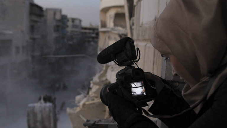 Skjermbilde fra filmen «For Sama». Kvinne filmer krigen i Syria.